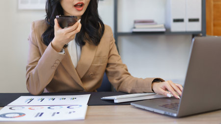 Secretary concept, Female secretary talking with the boss on smartphone and checking data on laptop.の素材