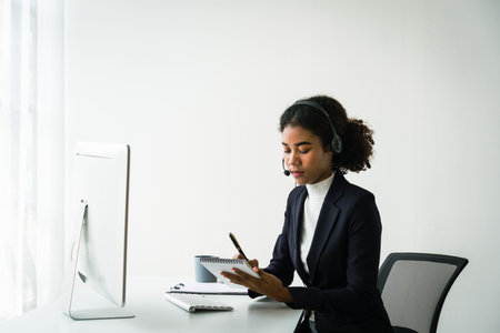 African american woman in headset writing notes while talking support customer in call center.の写真素材
