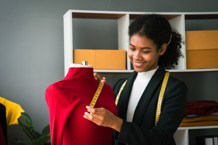 African american designer woman checking details and measuring the size of sweaters on mannequin.の写真素材