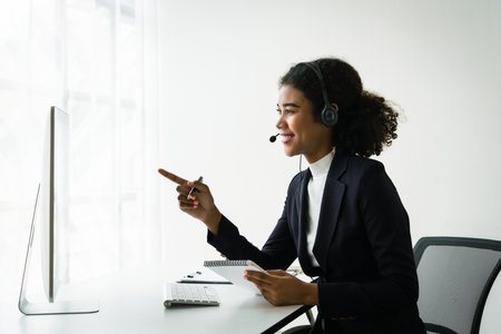African american woman in headset reads data on computer while talking with customer in call center.の写真素材