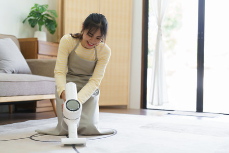 Maid using handheld cordless vacuum cleaner to vacuuming and cleaning the dust on carpet in home.の写真素材