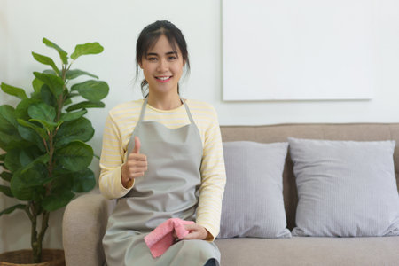 Maid holding microfiber fabric and showing thumb up after cleaning and wiping the dirty in home.