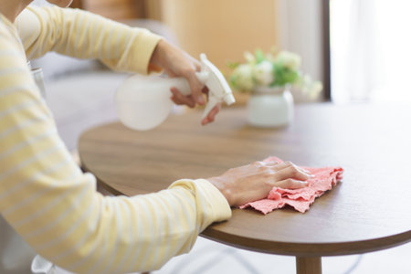 Maid spraying cleaner on wood table and wiping dirty with microfiber fabric to cleaning in home.の写真素材