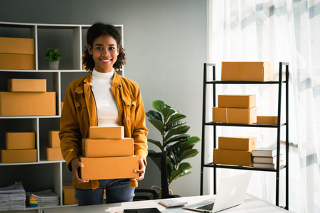 African american woman carrying parcel box for delivery to customer while working in home office.の写真素材