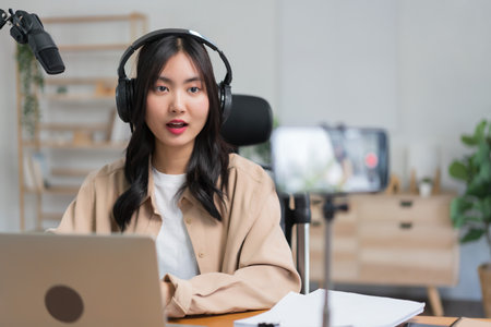 Female podcaster use smartphone and speaking with audience on microphone to recording video podcast.の写真素材