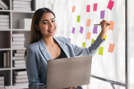 Businesswoman working on laptop and writing strategy ideas of new business project in sticky notes.の写真素材