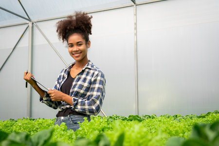 African american woman writing notes and examining quality of vegetables in hydroponics greenhouse.の写真素材