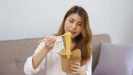 Work from home concept, Asian woman use chopsticks and eats instant noodles after successfully work.の写真素材