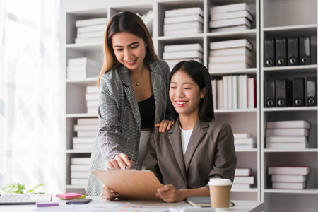Two businesswomen reads finance document to brainstorming strategy of new business project together.の写真素材