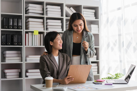 Two businesswomen reads finance document to brainstorming strategy of new business project together.の写真素材