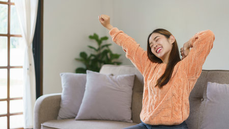Women raise arms to stretching and exercise while sitting on big sofa to relax in lifestyle at home.の写真素材