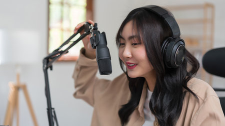 Female podcaster talking about news into microphone and recording audio podcast in broadcast studio.の写真素材