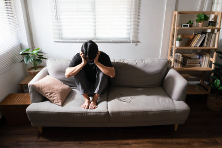 Man with mental health problem sitting on couch and use hands to covering ears from noise anything.の写真素材