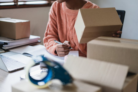 African american women hold parcel box and checking data on laptop to writing address for delivery.の写真素材