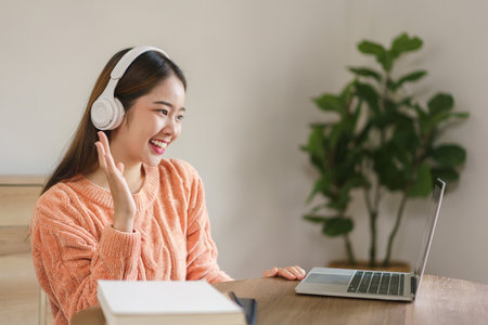 Women wearing headphone and greeting with friends in video call on laptop in lifestyle at home.