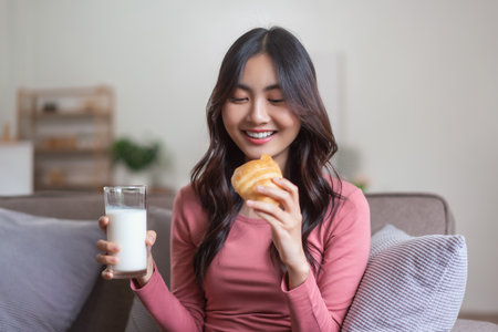 Women leisure on sofa to drinking milk and eating bread with healthy meal in lifestyle at home.の写真素材