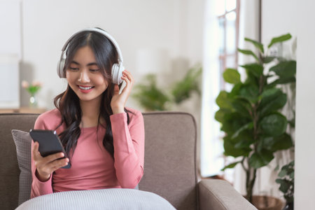 Women in headphone talking on video call with smartphone while leisure on sofa in lifestyle at home.の写真素材