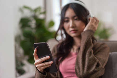 Women wearing headphones and watching movie with entertainment on smartphone in lifestyle at home.の写真素材