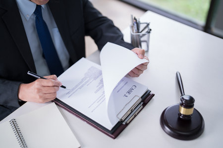 Male lawyer reading and checking financial document of business to analysis about legal agreement and terms of business contract while working on the desk with laptop technology in law firm.の写真素材