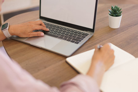 Female entrepreneur working at home to searching business data on laptop and writing notes in paper.