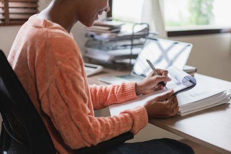 African american businesswoman writing notes and working about finance of business in workplace.