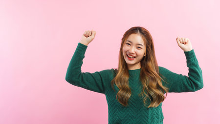 Young women raising arms with winner gesture and smiling with happiness isolated on pink background.