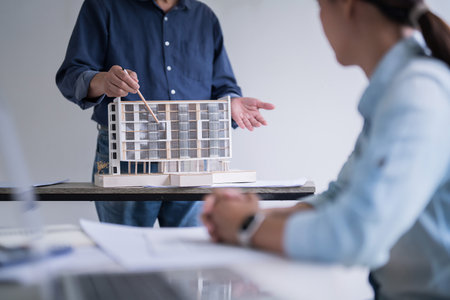 Male engineer architect pointing on building model to explaining about interior architectural building and construction plan to colleague while working analysis technical together in workplace site.の写真素材
