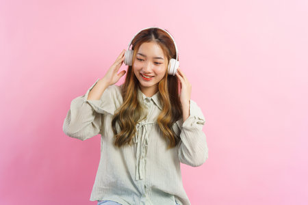 Young women wearing headphone to listening music with empty space on isolated pink background.の写真素材