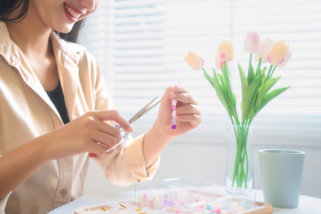 Young asian women use scissor with needlework while stringing colorful beads to making handmade...