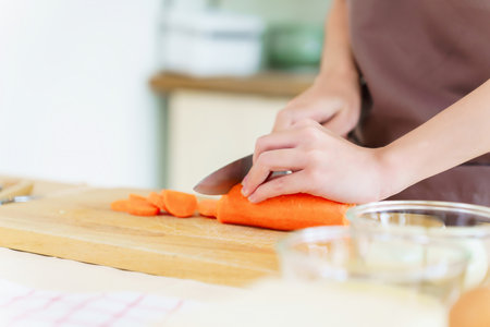 Closeup hands of asian women chopping slices carrot with knife on cutting board to preparing fresh vegetables of ingredients for cooking breakfast meal while making healthy food lifestyle in kitchen.の写真素材