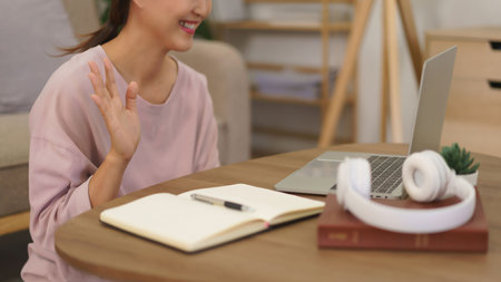 Female entrepreneur meeting and greeting with partner in video call on laptop while working at home.
