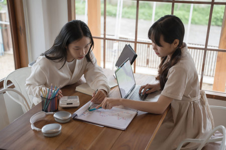Two businesswomen pointing on finance graph to checking financial statistics with calculator while brainstorming about investment of new project and enjoying with friendship conversation in workspace.の写真素材