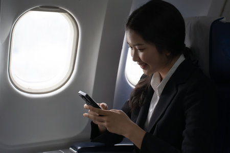 Businesswoman using smartphone to message chatting and working to reading financial business report while sitting near windows on flight business travel in airplane during vacation time lifestyle.の写真素材