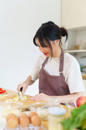 Asian women is chopping boil egg with knife on cutting board and slices fresh vegetables to preparing ingredients for cooking breakfast meal while making healthy food lifestyle in the kitchen at home.の写真素材