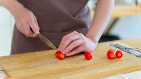 Asian women chopping slices tomatoes with knife on cutting board to preparing fresh vegetables of...