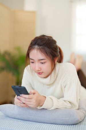 Young asian women in sweater lying on comfortable couch to enjoying with chatting social media on smartphone while relaxation and doing activity to spending time with slow life lifestyle at home.の写真素材