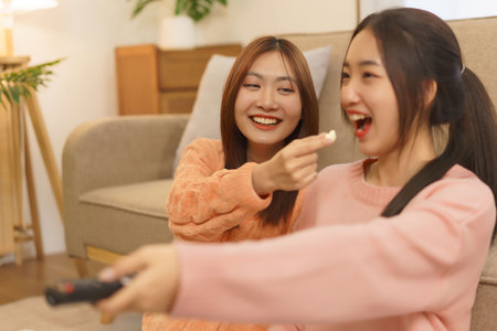 Friendship concept, LGBT lesbian couple feed popcorn to girlfriend while switching channels movie.の写真素材