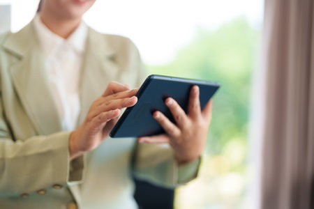A businesswoman in a light-colored suit stands at her desk, reading business information on her...