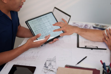 Engineers discussing construction plans at the desk with blueprints and calculators, focusing on...