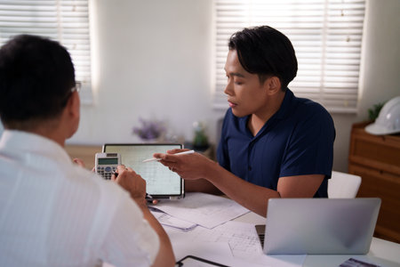 Engineers discussing construction plans at the desk with blueprints and calculators, focusing on project strategies and material estimates.の写真素材