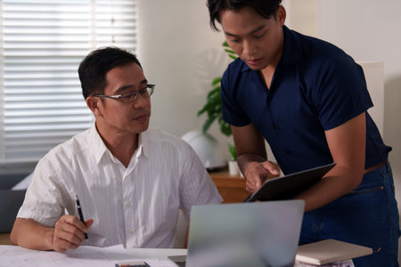 Two engineers analyzing a construction project's blueprint and taking notes on material usage.の写真素材