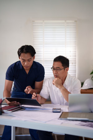 Two engineers analyzing a construction project's blueprint and taking notes on material usage.の写真素材