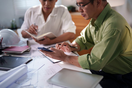 Engineers collaborating on project details with blueprints, material samples, and technical diagrams on the table.の写真素材