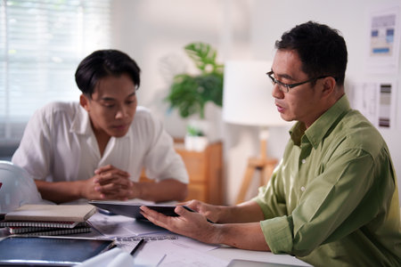 Engineers collaborating on project details with blueprints, material samples, and technical diagrams on the table.の写真素材