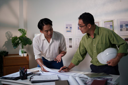 Engineers working together on construction project calculations, using blueprints, laptops, and technical tools at the meeting table.の写真素材