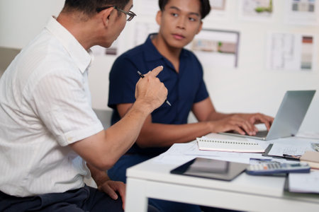 Engineers brainstorming construction ideas while referencing blueprints and material lists at the deskの写真素材