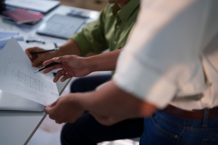 A team of engineers evaluating project risks and discussing construction timelines at their workspace.の写真素材
