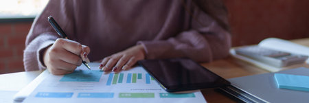 A young female designer in a casual sweater is working on design sketches and notes in a modern workspace with a brick wall background. She is focused and engaged in her creative process.の写真素材