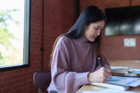 A young female designer in a casual sweater is working on design sketches and notes in a modern...