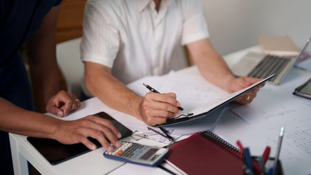Two engineers analyzing a construction project's blueprint and taking notes on material usage.の写真素材